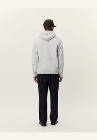 Sudadera gris con capucha y dobladillo acanalado, combinada con pantalones azul marino. Look casual en general, presentado desde la vista posterior.