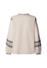 Kremna bluza z dolgimi rokavi z modrim in črnim geometričnim vezenjem na rokavih, manšetah in izrezu, prikazana od zadaj na ravni podlagi.