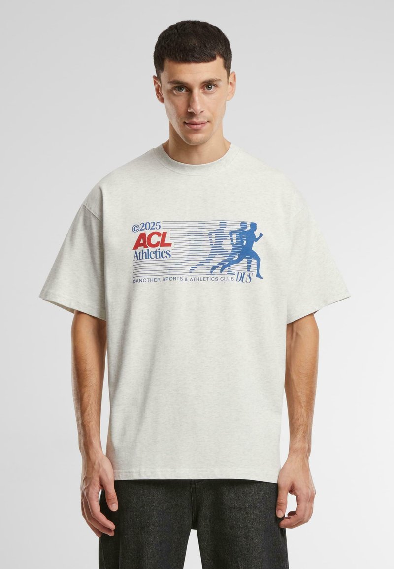 Tricou supradimensionat de un gri deschis, cu un design grafic albastru ce include figuri atletice și text, realizat dintr-un material din bumbac moale. Mâneci scurte.