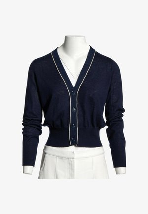 Cardigan court bleu marine à manches longues, boutonné devant, avec une bordure claire le long du col en V sur un mannequin blanc.