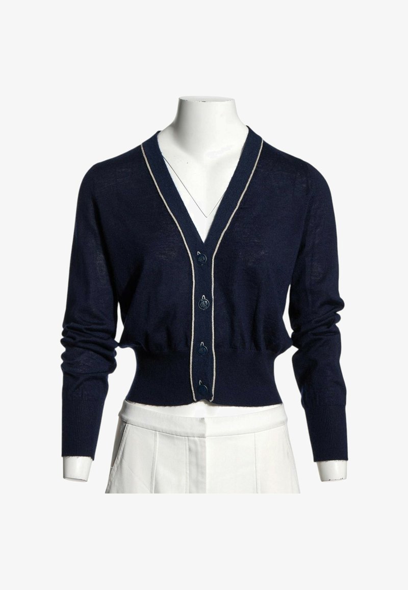 Cardigan court bleu marine à manches longues, boutonné devant, avec une bordure claire le long du col en V sur un mannequin blanc.