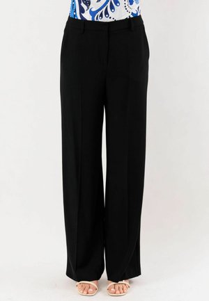 Pantaloni neri a gamba larga indossati da una persona con un top a motivi blu e bianchi e sandali beige con punta aperta su uno sfondo semplice.