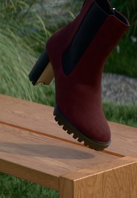 Burgundy Knöchelstiefel mit einer glatten Wildleder-Oberfläche, schwarzen elastischen Seiteneinsätzen und einer kräftigen schwarzen Sohle. Erhöhtes Design mit einem leichten Absatz.