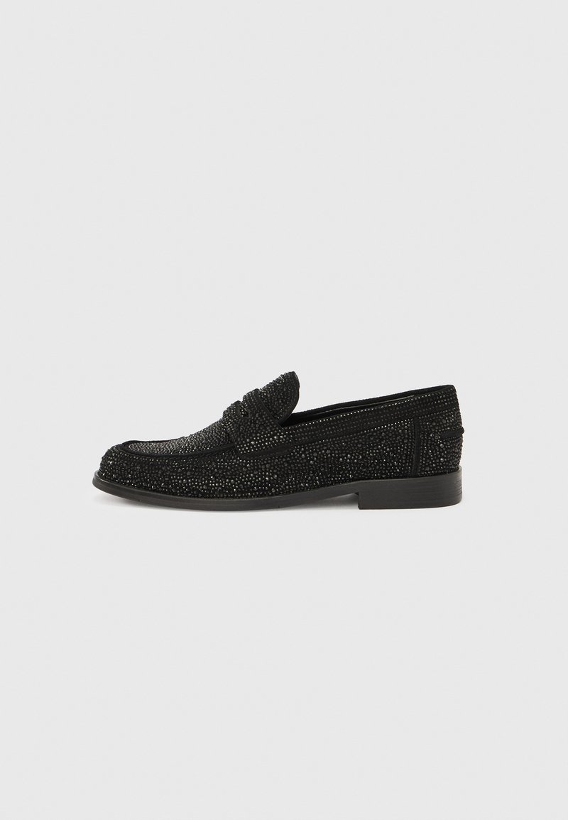 Mocassins noirs en tissu texturé, avec un petit nœud sur le devant et un talon plat, ornés de motifs complexes en perles sur toute la surface.