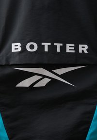 Black textile with a glossy finish, featuring large white "BOTTER" text and a silver Reebok logo design. Accented with turquoise sides.