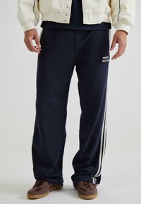 Mørkebl�å sweatpants lavet af blødt stof med sidelister og et logo, der står "PROHIBITED SOCIAL CLUB." Afslappet pasform for komfort.