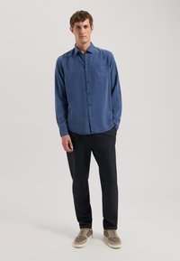 Cămașă albastră cu mânecă lungă, guler cu nasturi și buzunar pe piept, asociată cu pantaloni negri și teniși gri. Textură netedă și croi lejer.