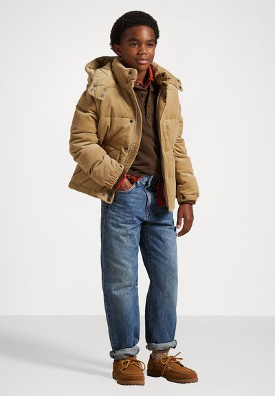 Casaco puffer de cordura castanho com capuz, combinado com uma polo castanha escura, jeans azuis e sapatos castanhos com atacadores. Design texturizado e casual.