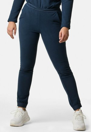 Laivansiniset fleece-housut, joissa on istuva muotoilu, sivutaskut ja texturoitu vyötärö. Yhdistetty valkoisten urheilujalkineiden kanssa.
