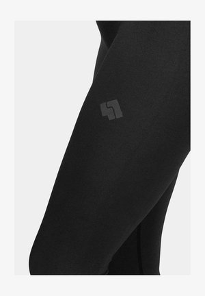 Czarne legginsy z elastycznego materiału charakteryzują się gładką fakturą i małym, subtelnym nadrukiem logo z boku.