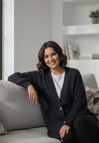 Granatowy sweter na drutach z fakturowanym wzorem, dużymi guzikami i ściągaczami na rękawach, noszony na białej koszuli, siedzący na jasnoszarej sofie.