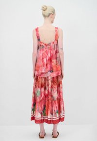 Farbenfrohes, gestuftes Maxikleid mit Spaghettiträgern. Es hat ein Blumenmuster in Rosa- und Grüntönen, abgerundet mit einem kontrastierenden Saum.