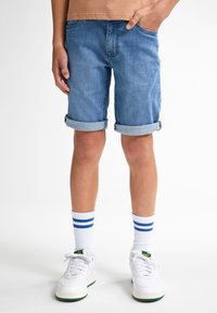 Shorts de mezclilla, azul claro, con dobladillo doblado, con cinco bolsillos. Combinados con zapatillas blancas y calcetines blancos con rayas azules.