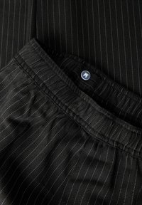 Sort pindtrækstof med elastisk talje og en blå knap detalje. Teksturen er glat med fine hvide striber.