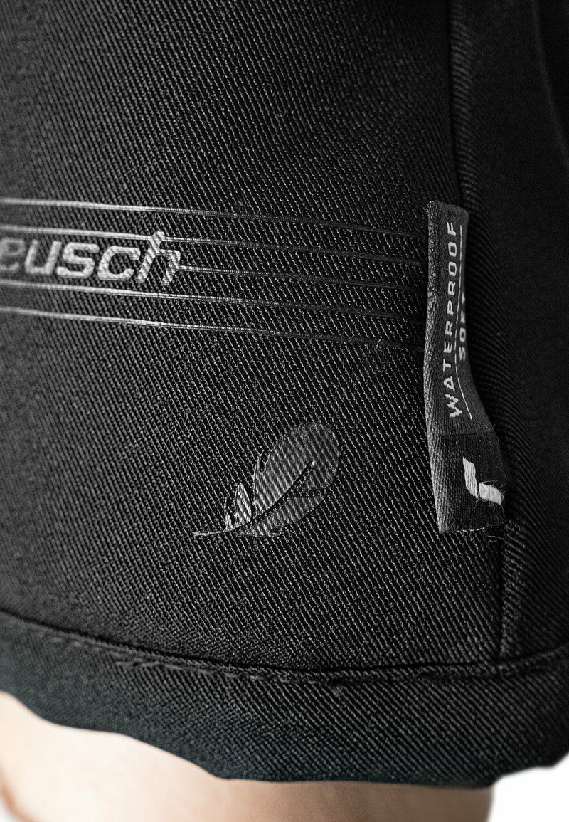 Schwarzer wasserdichter Stoff mit strukturierter Oberfläche, versehen mit einem Logo und einem Etikett, das die wasserabweisenden Eigenschaften anzeigt. Fein genähte Kanten.