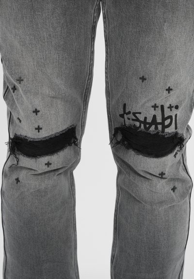 Erschöpfte graue Denim-Jeans mit aufgerissenen Knien, schwarzen ausgefransten Kanten und verstreuten schwarzen Pluszeichen. Der Markenname "tsubi" ist in Schwarz aufgedruckt.