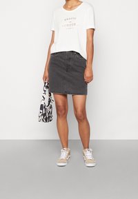 Grauer Denimrock, weißes T-Shirt mit goldener Schrift, gemusterte schwarz-weiße Tasche, beigefarbene Sneaker. Einfaches Design, lässiger Stil.
