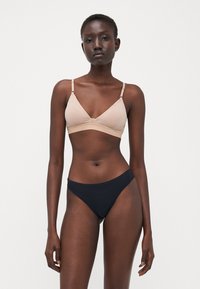 Lichtbeige bralette met dunne bandjes en V-halsontwerp, gecombineerd met zwarte high-waisted bikini bottoms. Glad materiaal, minimale naden.