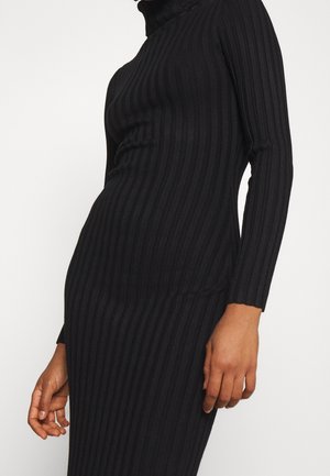 Schwarzes, geripptes Strickkleid mit langen Ärmeln und hohem Kragen, getragen von einer Person, die von der Brust bis zur Hüfte zu sehen ist.