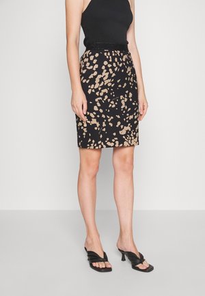 Femme portant un haut noir sans manches, une jupe noire longueur genou avec un imprimé abstrait beige, et des sandales à talons noires avec un design à bout ouvert.