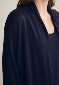 Navyblauer Cardigan aus weichem Strickstoff, mit einer lockeren Passform, offener Vorderseite und überschnittenen Schultern. Subtile Struktur sichtbar.