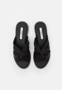 Svarta slide-sandaler med en knutig tygövre och strukturerad sula, med en nitar trim runt kanterna för extra detalj.