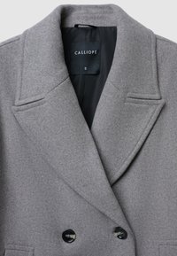 Grau melierter, doppelt knöpfbarer Mantel mit großen Revers, zwei schwarzen Knöpfen und einer Tasche, ausgestattet mit einer schwarzen Innenauskleidung und einem Etikett.