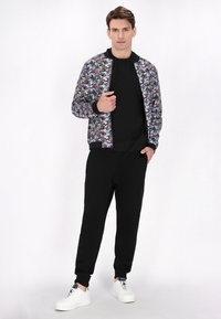 Bomberjack met een veelkleurig abstract patroon, zwart jersey shirt, zwarte joggers en witte sneakers. Voorzien van geribbelde manchetten en tailleband.
