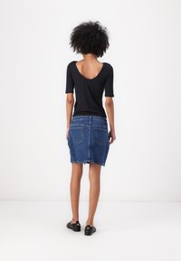 Svart t-skjorte med korte ermer og scoop-back, kombinert med en blå denim miniskjørt med to baklommer og ujevn kant. Sorte sko.
