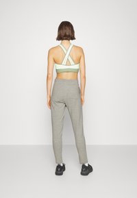 Light green sports bra with a crisscross back design and mesh accents, paired with gray tapered sweatpants and black athletic shoes.