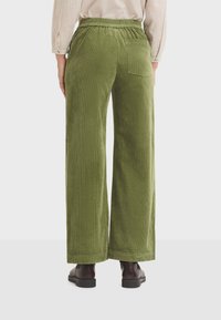 Green corduroy wide-leg pants with an elastic waistband and back pocket, shown from the back. Paired with dark brown ankle boots.