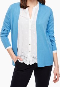 Světle modrý kardigan s dlouhými rukávy, otevřeným předním dílem, žebrovanou strukturou a bočními kapsami. Pod ním bílá vyšívaná blůza s knoflíkovou légou.