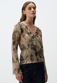 Langärmlige Bluse aus geripptem Stoff mit floralem Muster, V-Ausschnitt und Rüschensaum. Die Farben umfassen Beige, Schwarz und gedämpfte Rottöne.