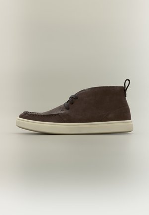Bottine en daim marron foncé avec semelle en caoutchouc crème et lacets noirs, vue de profil sur un fond neutre.