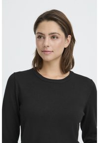 Pull noir en maille avec un col rond, des manches longues et une texture lisse, présentant des détails de coutures subtils sur les épaules.