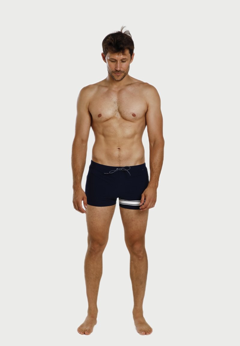 Marineblaue Badeshorts mit einem Kordelzug, ausgestattet mit horizontalen Streifen in Weiß und Silber am unteren Rand. Glatte Stoffoberfläche.