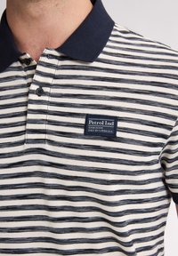 Pruhovaná polo košile v krémové a navy barvě, s knoflíkovým límečkem, malou nášivkou loga a texturovanou tkaninou s mixem pruhového vzoru.
