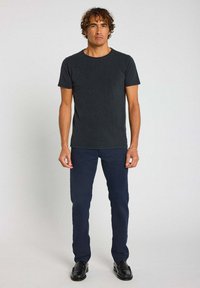 T-shirt en coton gris foncé à manches courtes, associée à un pantalon bleu marine et des chaussures noires. Design simple et silhouette ajustée.