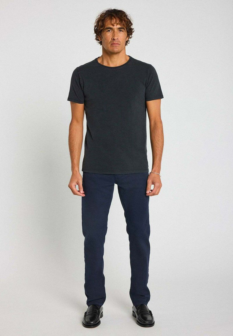 T-shirt en coton gris foncé à manches courtes, associée à un pantalon bleu marine et des chaussures noires. Design simple et silhouette ajustée.