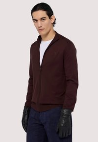 Vínová bunda na zip, hladká látka, přiléhavý střih, doplněná černými koženými rukavicemi, model má pod bundou bílou košili.