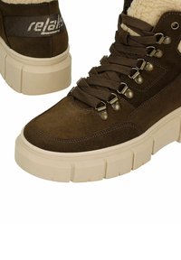 Bruine suède hoge sneakers met een dikke beige rubberen zool, met metalen oogjes, veters aan de voorkant en een logo bij de enkel. Voering van nepbont.