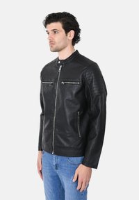 Giubbotto da motociclista in pelle nera con colletto alto, tasche con zip, dettagli a coste sulle spalle e una silhouette aderente.
