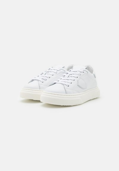 Baskets blanches avec un haut en cuir lisse, un design à lacets, un col rembourré et une semelle en caoutchouc texturée. Style minimaliste.
