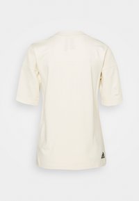 Světle béžové sportovní tričko s krátkými rukávy, kulatým výstřihem a malým černým logem v dolním levém rohu. Hladká, jemná textura.