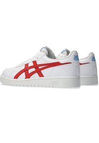 Białe buty sportowe z czerwonymi akcentami i niebieskim logo, z teksturowaną skórzaną cholewką oraz trwałą gumową podeszwą z rowkami.