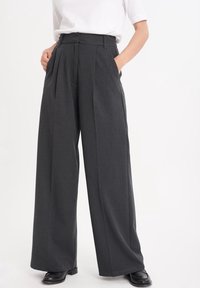 Höga, vida byxor i mörkgrått tyg. Har veck, bälteshällor och sidofickor. Mjuk yta med en skräddarsydd finish.