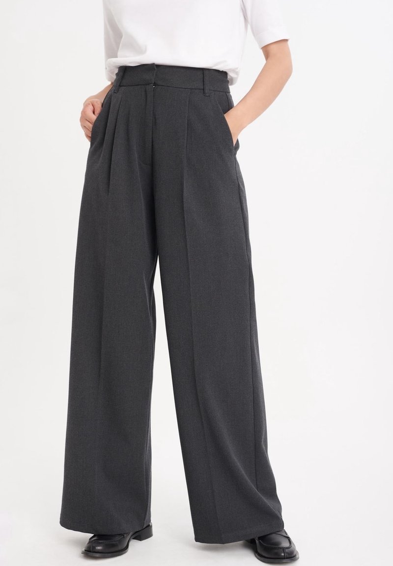 Höga, vida byxor i mörkgrått tyg. Har veck, bälteshällor och sidofickor. Mjuk yta med en skräddarsydd finish.