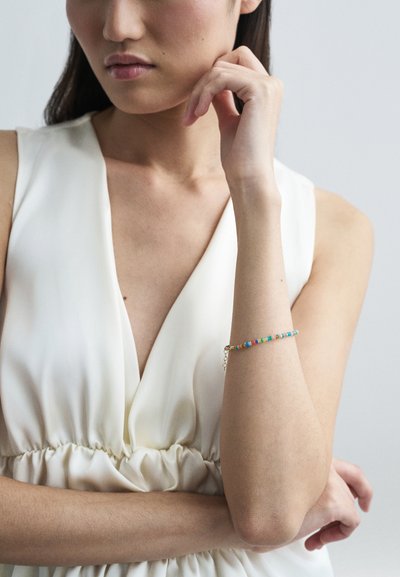 Erinevate värvidega helmedest valmistatud käevõru kuldsete detailidega. Kandmine palja käsivarre peal, koos valge V-kaelusega kleidiga.