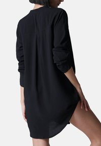 Zwarte langemouwen shirt met een relaxed fit, voorzien van een rug yoke detail, verlaagde schouders en zijsplitten voor gemakkelijke beweging.