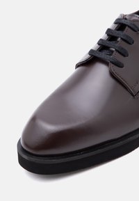 Κοντινό πλάνο σκούρου καφέ δερμάτινου παπουτσιού φόρεμα με μαύρα κορδόνια και χοντρή μαύρη σόλα σε λευκό φόντο.